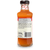 Back view of a small glass bottle of Kame's Sauce with orange-red sauce inside, a black cap, and a white product information label.
