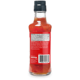 Back view of a hot sauce bottle showing the ingredients label, with red sauce visible through the clear glass and a black cap, on a white background.