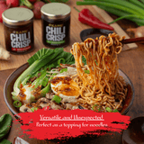 Bowl of noodles with chili crisp toppings on a wooden table, featuring two jars of chili crisp.